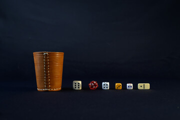 Variety of Colorful Dice and a Wooden Cup Against a Dark Background