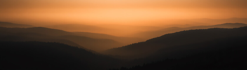 A serene landscape showcasing gentle hills gradually fading into the horizon, bathed in warm hues of orange and soft shadows, creating a tranquil, dreamy atmosphere at sunset.