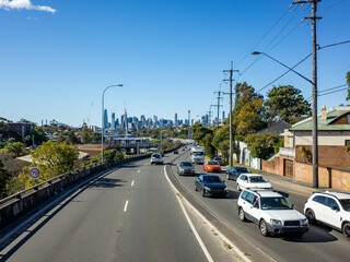 Elevated view of a busy suburban road leading towards the Sydney city skyline, with modern high-rise buildings in CBD in the distance