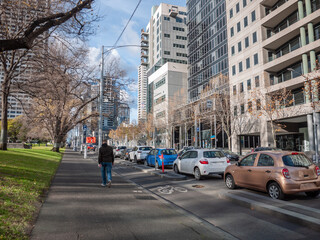 Urban street along Melbourne's La Trobe street with modern high-rise apartment and office buildings, parked cars, bike path and a pedestrian walking on a footpath © Doublelee