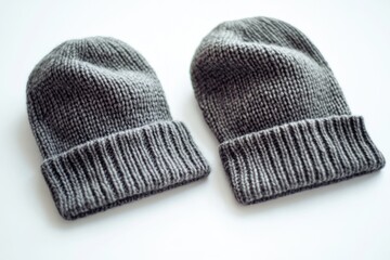 A pair of gray knitted hats sit on top of a table, waiting to be used or stored