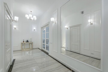 The corridor of a private house, decorated in neoclassical style. A large mirror, a double-leaf door with glass windows.