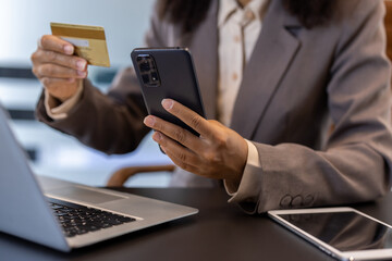 Hands of young African American woman sitting in office at desk with laptop, using mobile phone and credit card