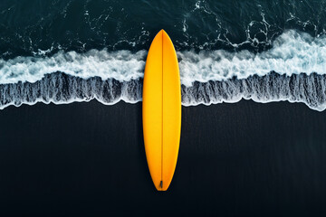 Shot from above, drone shot of a yellow surfboard on a black sand beach, with crashing waves in the background
