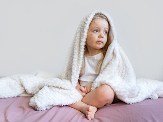 Chickenpox in a little child. Portrait of a little girl with a blanket on her head with a rash from...