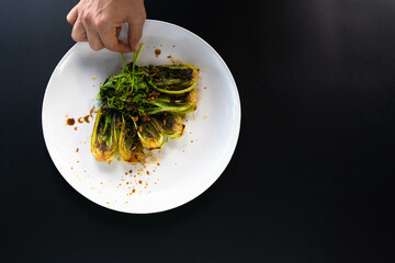 Hand is garnishing bok choy with spices in an Asian kitchen, showcasing preparation.
