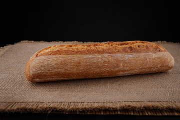 Baguette, a loaf of bread lies on a burlap napkin. Side view.