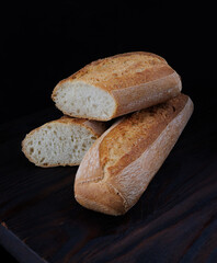 Fresh hot bread. Two loaves of baguette on a black background. Sliced bread.