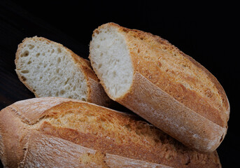 Fresh hot bread. Two loaves of baguette on a black background. Sliced bread.