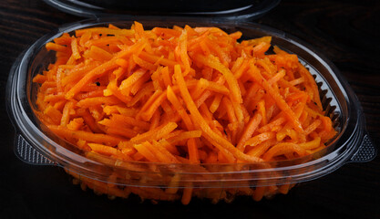 Korean spicy carrot salad in plastic container on dark background.
