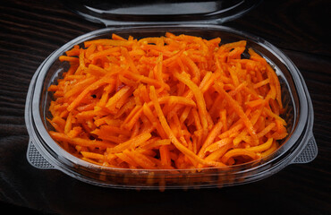 Korean spicy carrot salad in plastic container on dark background.