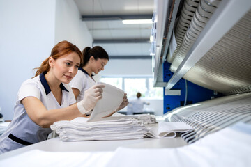 Obraz premium Female laundry workers folding linen and bedsheets after ironing in dry cleaning service.