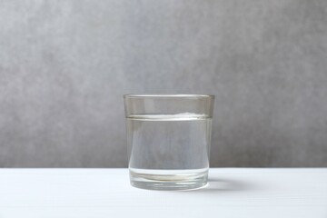 Glass with clear water on white table, space for text