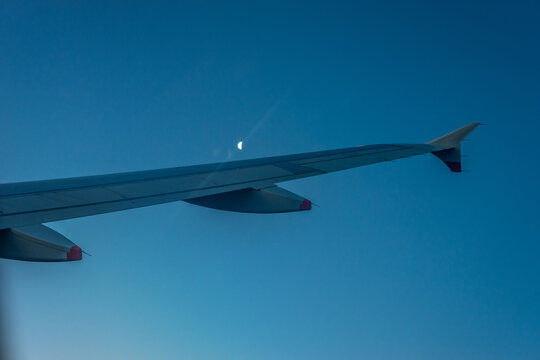 A view of an aeroplane wing with a crescent moon in the background