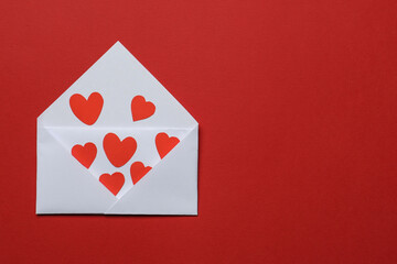 Valentine's Day. Envelope with many paper hearts on red background, top view. Space for text