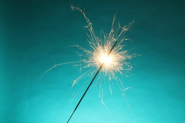 Bright burning sparkler on turquoise background, closeup