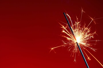 Obraz premium Bright burning sparkler on red background, closeup. Space for text