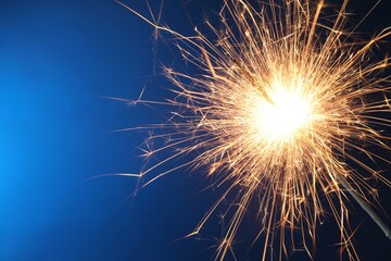 Obraz premium Bright burning sparkler on blue background, closeup. Space for text