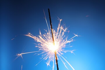 Bright burning sparkler on blue background, closeup