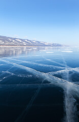 Beautiful winter landscape of frozen Baikal Lake on sunny February day. Small Sea is covered with clear transparent blue ice with cracks. Natural background. Winter travels. Empty space for text