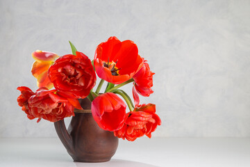 A bouquet of red tulips in a clay jug on a light background. Copy space