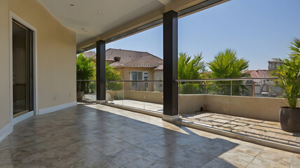 Luxury Patio Oasis: Sun-drenched luxury patio with stone flooring, modern glass railings, and dark pillars offering a tranquil view of a lush, green neighborhood.