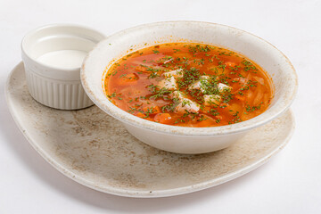 Warm and Hearty Bowl of Vibrant Soup Garnished With Fresh Herbs Served Alongside a Small Dish of Cream for a Comforting Meal Experience