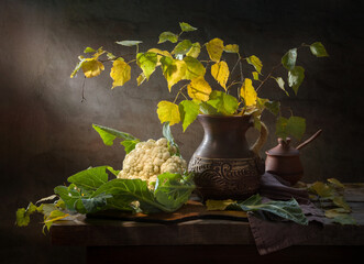 Village still life with a bouquet of birch branches in a clay jug and cauliflower on a dark...