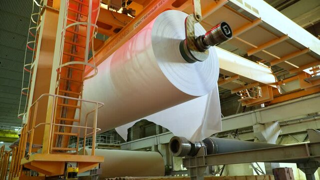 A railway overhead crane transports a roll of white paper. Paper production