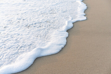 Close-up of a coral sand beach with white sea foam washing up and resting on the surface.