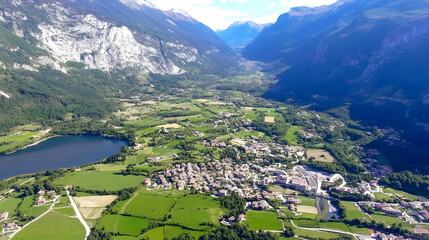 Aerial view over houses, lake, and green fields in a sunny valley surrounded by mountains for travel, tourism, or exploration concepts