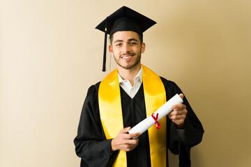 Proud graduate smiling and showing his diploma at graduation ceremony