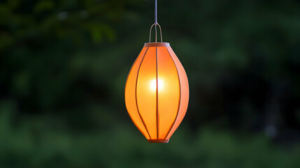 Lit orange lantern hanging outdoors illuminating space against blurred trees at twilight. For decoration, celebrations or garden events