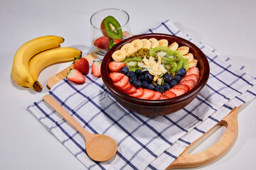 A vibrant and healthy smoothie bowl topped with fresh strawberries, blueberries, kiwi, banana slices, almonds, and pistachio. Placed on a wooden board.