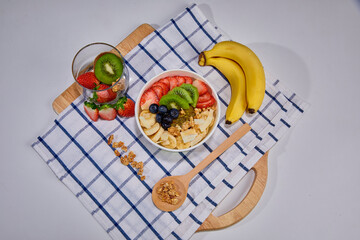 A vibrant and healthy smoothie bowl topped with fresh strawberries, blueberries, kiwi, banana slices, almonds, and pistachio. Placed on a paper cup.