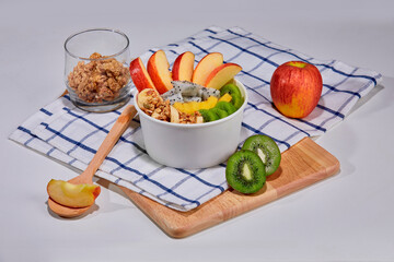 A delicious and nutritious granola bowl topped with fresh apple, kiwi, banana slices, coconut flakes, and almonds. Placed on a wooden board with a checkered napkin.