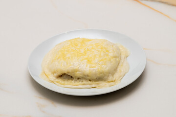 a plate of cannelloni, with bechamel sauce on top and gratin cheese on a white plate on a white veined marble table