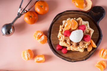 Belgian waffles with berries and tangerines on a pink background. Viennese waffles with a scoop of ice cream for dessert. View from above. Close-up