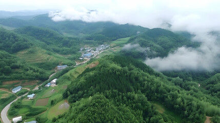 Fototapeta premium Aerial view of valley with rolling hills, clouds, and village nestled in the valley. Potential use Stock photo for travel, landscapes, and nature-related imagery
