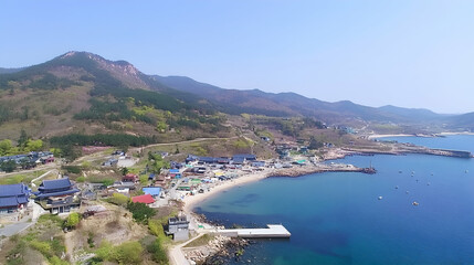 Fototapeta premium Aerial view of coastal village nestled beside mountains. Possible use Stock photo for travel guides, tourism websites, or showcasing Asian villages