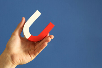 Man holding horseshoe magnet on blue background, closeup. Space for text