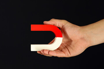 Fototapeta premium Man holding horseshoe magnet on dark background, closeup