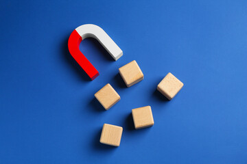 Magnet attracting wooden cubes on blue background, top view