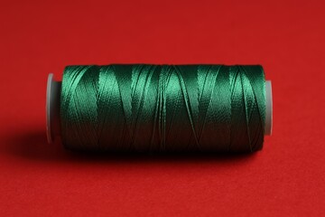 Spool of green sewing thread on red background, closeup