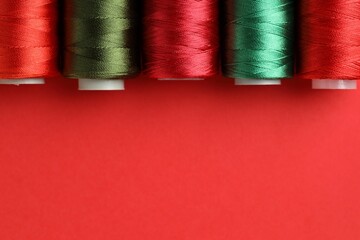 Different spools of sewing threads on red background, flat lay. Space for text
