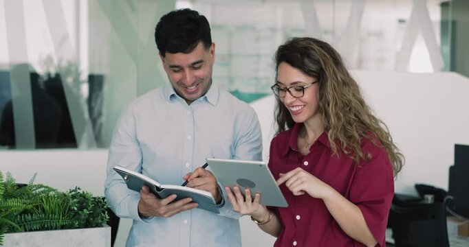 Woman hold tablet engaged in teamwork with colleague, provide details and explanation. Man writing notes in personal organizer, review data, brainstorm ideas, or planning tasks with female teammate