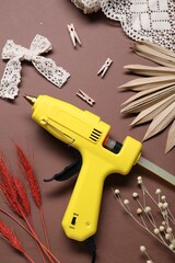 Hot glue gun and handicraft materials on brown background, flat lay