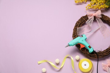 Hot glue gun and handicraft materials on lilac background, flat lay. Space for text