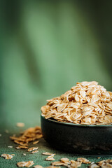 A bowl filled with rolled oats on a green textured background. Minimalistic and natural food composition, highlighting healthy eating, breakfast, and organic ingredients in a cozy, soft light setting