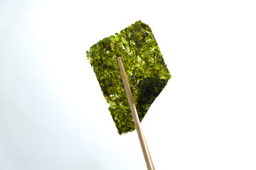 Crispy nori seaweed on white background with clipping path. Chopsticks hold a piece of crispy dried seaweed isolated on white background. Dry seaweed sheets.